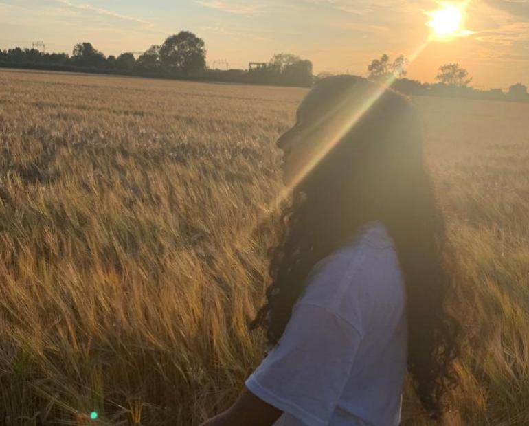 A girl walking on a field with a golden sunset. 