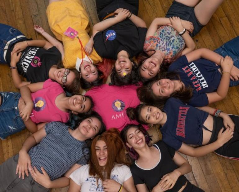 Grupo de chicas recostadas en el piso en forma de círculo, rodeando una polera con el logo de AMUJI Chile.