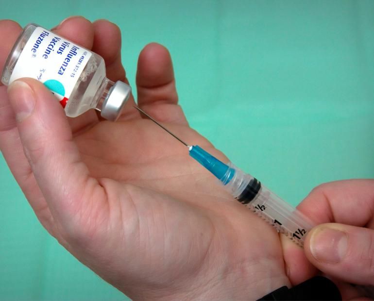 A close view of person hands, holding the vaccine vial with her left hand, and using a syringe, extracting the vaccine dose, with her right.