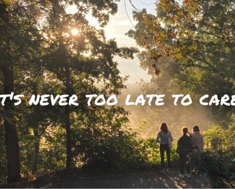 The image shows 3 people standing in a forest, facing the sunlight on the few enlightened places between the trees. The title “it’s never too late to care” is displayed over it in white.