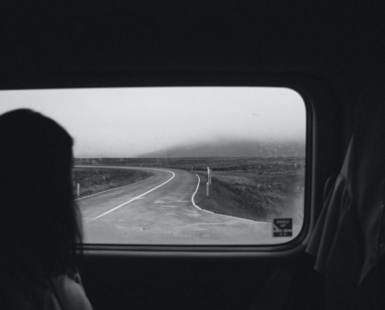 Una joven mirando por el parabrisas trasero de un auto a un camino de tierra.