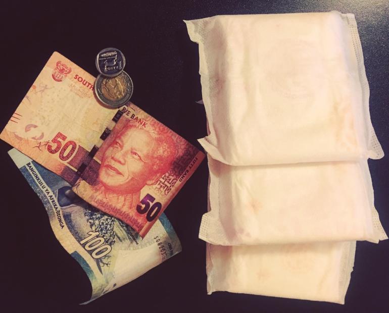 Three Menstrual Pads, One-hundred Rand South African Notes, Fifty Rand South African Notes, Five Rand South African Coin, One Rand South African Coin on a Black Surface