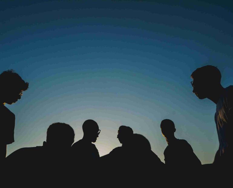 The silouettes of a group of young people, the sky turning dark behind them.