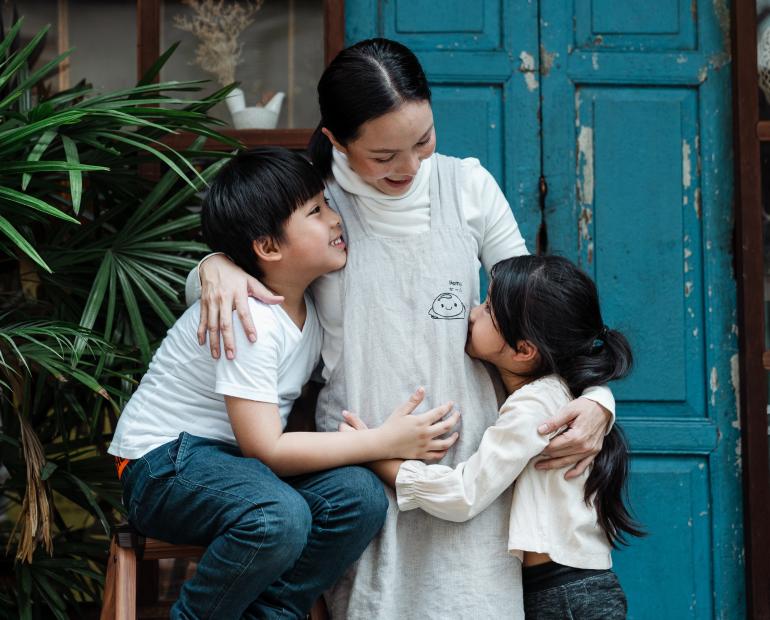 A mother comforting her son and daughter by holding them close to herself.