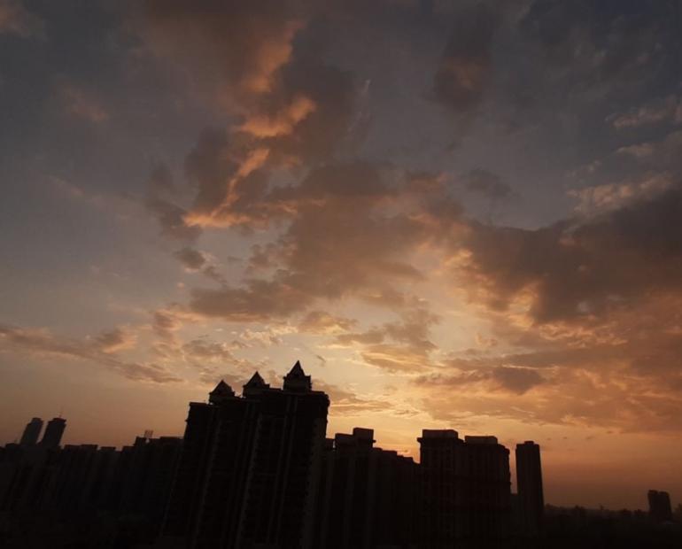 A beautiful sky, with splashes of cyan blue and light orange, accompanied by soft, scattered clouds. A silhouette of buildings marries into the scene.