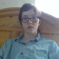 A boy with a blue shirt sitting on his bed.