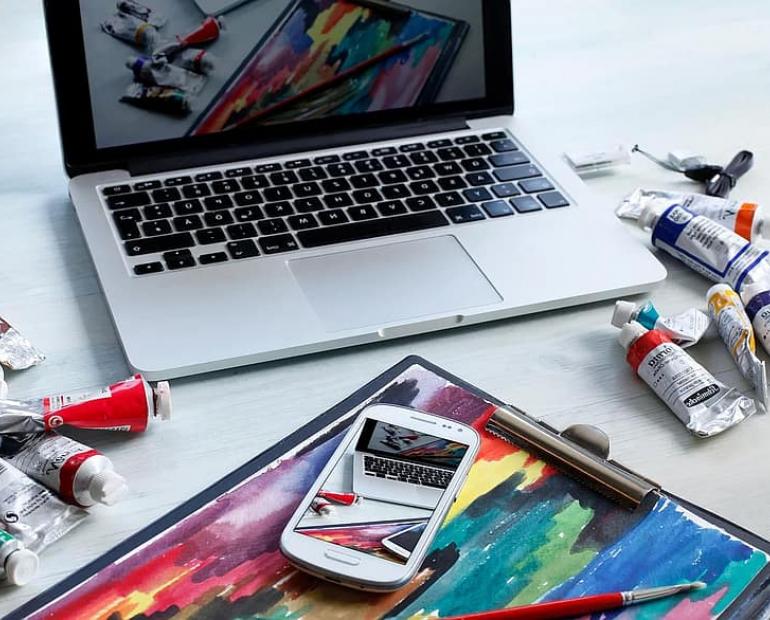 A computer and a table strewn with painting supplies