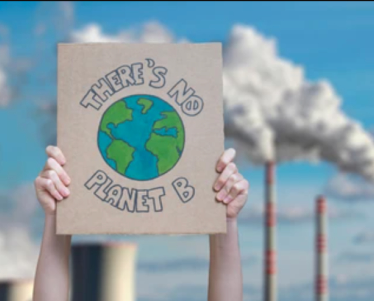 Person holding up sign that says "There's no planet B" in front of a carbon-emitting factory